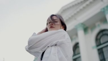 Mimari bir zemine karşı modern beyaz bir elbise giymiş genç bir kadının çarpıcı bir görüntüsü. Bakış ve duruş kendine güven ve stili çağrıştırıyor. Şık Giyimli Kendine Güvenen Genç Kadın