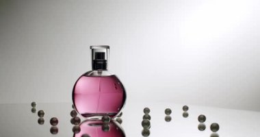 Zarafet ve lüksü yansıtan bir yüzeyde dağınık incilerle çevrili güzel tasarlanmış pembe bir parfüm şişesi. Yansıtıcı Yüzeyde Mor Sıvı ile Zarif Parfüm Şişe