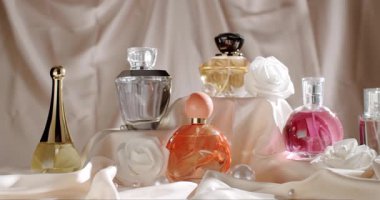 Dekoratif beyaz çiçekler ve lüks saten kumaşlarla sergilenen zarif parfüm şişeleri sofistike ve romantik bir atmosfer yaratıyor..