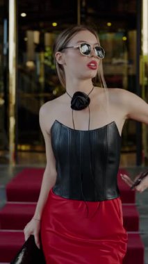 Siyah deri korse ve kırmızı etek giyen, güneş gözlüğü takan, kendine güvenen zarif bir kadın. Şık ve şık moda açık havada yakalanmış gibi. Dikey video.