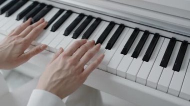 Tamamen beyaz bir ortamda piyano çalan, hassasiyet ve zarafet sergileyen bir kişinin yakın çekimi. Müzik, yaratıcılık ve konsantrasyon konuları için mükemmel. Eller Piyano Anahtarları Çalıyor