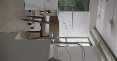 Modern ofis içi parlak beyaz sandalyeler ve minimalist çalışma alanı manzarası. Geniş pencereler doğal ışık sağlıyor ve davetkar bir atmosfer yaratıyor. Dikey video.