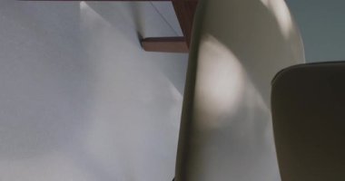 Zarif bir minimalist iç mimari detayı bir sandalye ve ahşap bir masanın ince çizgilerine odaklanarak sakin bir ortam yaratıyor. Zarif Sandalyesi ve Masası olan Minimalist İç Tasarım. Dikey video.