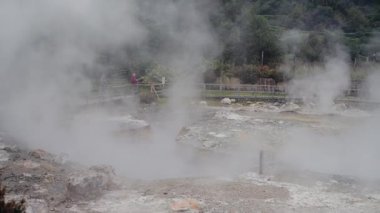 Portekiz 'in yemyeşil ve kayalık arazileriyle çevrili volkanik bir alanından yükselen jeotermal buhar. Puslu bir atmosfer ve manzarayı izleyen insanlar..
