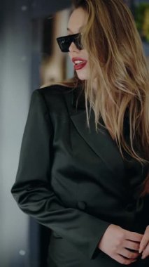 Siyah takım elbiseli ve güneş gözlüklü zarif bir kadın şehir ortamında kendine güven ve tarz yayıyor. İş, moda ve yaşam tarzı konuları için mükemmel. Siyah elbiseli, güneş gözlüklü genç bayan.
