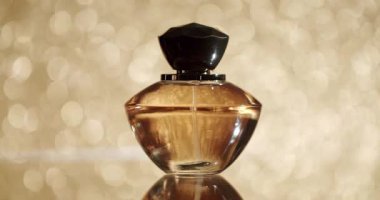Işıldayan altın bokeh arka planına karşı koyu şapkalı lüks bir parfüm şişesi zarafet ve inceliği çağrıştırıyor. Parıldayan Altın Arkaplan Karşısında Zarif Parfüm Şişe