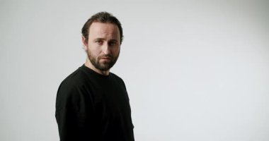Beyaz arka planda siyah tişörtlü bir adam başını çevirir ve kameraya ciddi bir ifadeyle bakar. Güven, profesyonellik ve farkındalık taşır..