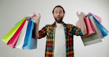 Mutlu adam beyaz arka planda renkli alışveriş torbaları tutuyor. Gülümsüyor ve alışverişleriyle poz veriyor. Bu video neşe, memnuniyet ve tüketim duygusunu çağrıştırıyor. Perakende ve satış için ideal,