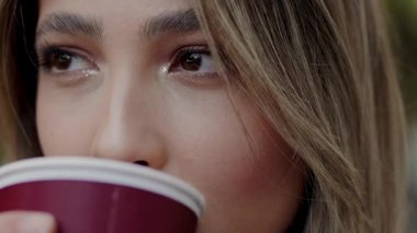 Stüdyoda, elinde kahve fincanı tutan, etkileyici gözleri olan genç bir kadının yakın çekim portresi. Kalabalık bir şehir yaşamında arka plan ipuçlarına yumuşak bir şekilde odaklan. Kahvesini yudumlayan Bir Kadının Yakın Çekim Portresi