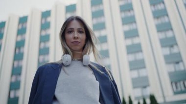 Genç bir kadın şehir ortamında kendine güvenir, kulaklık takar, modern yaşam tarzı ve bağlantıyı sembolize eder. Şehirdeki Genç Kadın Boynunda Kulaklıkla