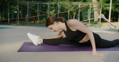 Siyah giysili güzel bir kadın yoga egzersizi yapıyor. Esnek, ince, genç bir kız antrenman yapıyor. Yoga yaparken bacaklarını açan sakin bir kadın. Sağlıklı yaşam tarzı kavramı.