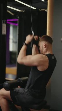 Genç bir adam modern bir spor salonunda son çekimleri yapıyor. Egzersizine odaklanmış durumda ve formunu geliştirmeye kararlı. Spor salonu iyi donanımlı ve motive edici bir atmosferi var..