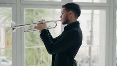 Takım elbiseli genç ve yakışıklı bir adam arzu ve ilhamla trompet çalar. Modern bir stüdyonun penceresinin yanında trompet çalan bir erkek caz şarkıcısı..