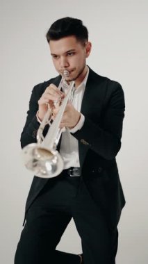 Takım elbiseli genç ve yakışıklı bir adam arzu ve ilhamla trompet çalar. Müzik tutkusu. Genç trompetçinin yakın eli. Müzik odası. dikey video.