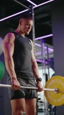 Kaslı bir adam modern bir spor salonunda halterle kaldırma işlemi yapar. Ağırlığı kaldırırken şekline ve gücüne odaklanıyor. Spor salonlarının mor ışıkları sahneye şık bir dokunuş katıyor..