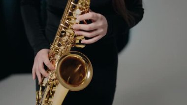 Siyah elbiseli genç bir kadın stüdyoda beyaz arka planda saksafon çalıyor. Romantik müzik. Saksafon çalan genç bir bayan müzisyen. Modern stüdyoda saksafon çalan bir kadın..