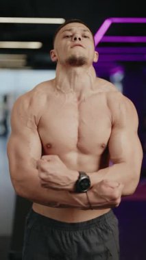 Kaslı adam fiziğini gösteriyor ve modern bir spor salonunda neon ışıklı kaslarını esnetiyor. Nefes veriyor ve ip atlıyor. Spor, spor, vücut geliştirme ve spor projeleri için ideal..