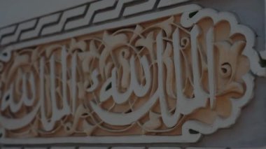 Fas duvarına karmaşık bir şekilde oyulmuş Arapça el yazısı yakın plan. Yazı, muhtemelen dini bir ayet, Fas kültüründe İslami sanatın ruhani bir anlamı..