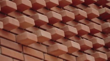 Eşsiz bir tasarıma sahip desenli tuğla bir duvarın yakın çekimi. Tuğlalar dışa doğru çıkıyorlar, dinamik, üç boyutlu bir model yaratıyorlar. Bu mimari detay görsel ilgi ve derinlik ekler.
