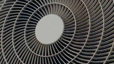 Dönen bir vantilatörün yakın çekimi, muhtemelen havalandırma ünitesinin bir parçası. Vantilatör pervaneleri düzgün dönüyor ve görüntü bulanıklığı yaratıyor. Beyaz vantilatör daha koyu bir arkaplanda zıtlaşıyor.