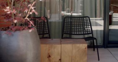 Modern otel ya da restoranda boş bahçe sandalyeleri ve masa seti. Siyah metal sandalyeler ve hafif ahşap masa misafirleri rahatlamaları için davet ediyor. Tenceredeki büyük bitki rahatlatıcı atmosfere katkı sağlar..