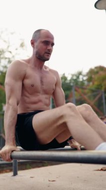 Kaslı bir adam açık hava spor salonunda paralel barlara daldırır. Egzersizine odaklanıyor. Gücünü ve forma bağlılığını gösteriyor. motivasyonel atmosfer.