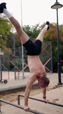 Olgun bir adam parktaki paralel parmaklıklarda amuda kalkar. Bu, güç, zindelik ve dengeyi gösterir. Açık havada sakin bir ortamda atletizm ve beceri sergiliyor..