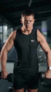 Kas yığını bir adam, spor salonunda dambıllarla yanal yükseltme yapar. Odaklanmış ve kararlı, sınırlarını zorluyor. Fiziğinde uygunluğa olan bağlılığı çok açık..