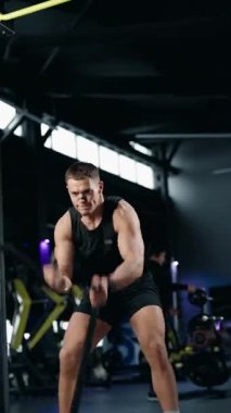 Kaslı bir adam spor salonunda ip çarpar. Odaklanmış ve kararlı, sınırlarını zorluyor. Spor salonu modern ve iyi donanımlıdır. Fitness, egzersiz ve spor içeriği için mükemmel..