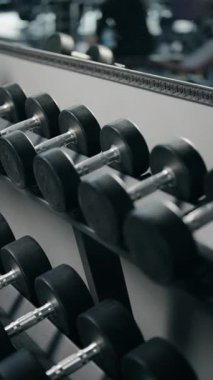 Spor salonunda dambıl seçen birinin yakın plan çekimi. Atış ağırlıkları vurguluyor ve insanların elleri onlara uzanıyor. Spor salonu arka planda görülebilir, fitness teması.