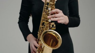 Siyah elbiseli genç bir kadın stüdyoda beyaz arka planda saksafon çalıyor. Romantik müzik. Genç bayan müzisyen saksafon çalıyor..