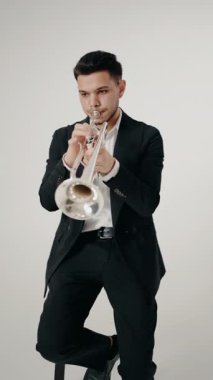 Modern bir stüdyoda beyaz arka planda trompet çalan bir erkek caz şarkıcısı. Canlı caz konseri. Müzik tutkusu. Genç trompetçinin yakın eli. Müzik odası. dikey video.