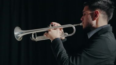 Takım elbiseli genç bir adam arzu ve ilhamla trompet çalar. Modern bir stüdyoda siyah arka planda trompet çalan bir erkek caz şarkıcısı. Genç trompetçinin eli.
