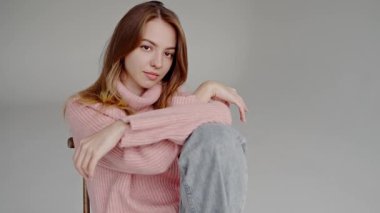 Yumuşak pembe balıkçı yaka giyen, tarafsız bir arkaplanda zarafetle poz veren kendine güvenen genç bir kadının portresi. Pembe boğazlı, kendine güvenen genç kadın zarif pozlar veriyor.