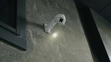 Beyaz bir güvenlik kamerası bir pencerenin yanında ve bir çatı kapısının altında seramikli bir duvara monte edilir. Bu küçük ışık, çevreyi aydınlatıyor. İzleme ve güvenlik hissi veriyor..
