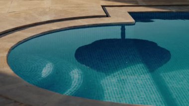 Sakin mavi havuz suyu güneşli bir günde bir şemsiyeyi yansıtır. Bu davet sahnesi rahatlama, yaz havası ve tatil mutluluğunu çağrıştırıyor. seyahat, eğlence, ya da yaşam tarzı projeleri.