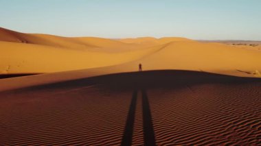 Sahra Çölü 'nün engin genişliği. Gün doğumunda güzel kum tepeleri. Kum tepeleri boyunca uzanan yalnız bir figür, bu Fas manzarasının güzelliği.