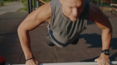 Bir adam açık hava parkı ortamında paralel barlar üzerinde yoğun bir egzersiz yapıyor. Görüntü, doğal bir ortamda zindelik, kararlılık ve sağlıklı yaşam tarzının özünü yakalar..