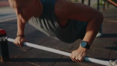 Formda bir adam açık hava spor aletleri üzerinde şınav çeker. Parlak, güneşli bir günde bir fitness parkında güç ve adanmışlık gösterir. Atletik Adam Spor Parkı 'nda şınav çekiyor.