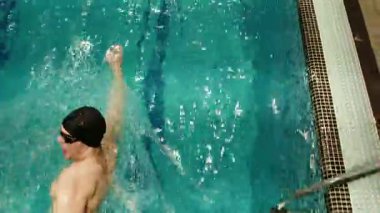 Kapalı Havuzda Serbest Yüzen Adam, Parlak ve Enerjik. Erkek bir yüzücünün yüzme havuzunda serbest stil vuruşunu kullanarak hareketliliği ve canlılığı vurguladığı dinamik bir görüntü..