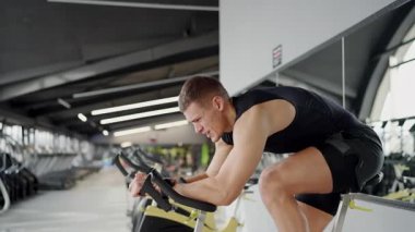 İyi donanımlı, çağdaş bir spor salonunda kürek çekme makinesinde yoğun egzersiz yapan kendini adamış ve formda olan genç bir adam. Modern Spor Salonunda Sıkı Çalışan Genç Adam.