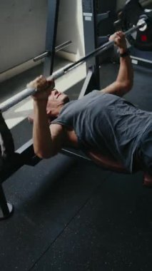 Sporcu, spor salonunda ağırlık kaldırma halterini kaldırarak antrenman yapıyor. Görüntü fitness, adanmışlık, güç ve sağlığı gösteriyor. Spor salonunda halterle çalışan adam dikey.