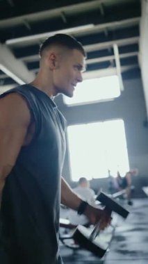 Spor salonunda dambılları kaldıran, parlak bir çevrede azim ve güç gösteren formda bir adam. Dambıllarla Spor Salonu 'nda Motivasyon İfadesiyle Çalışan Adam. Dikey