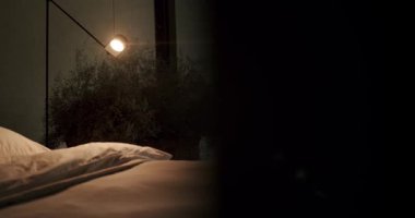 Davetkar bir yatak odası sahnesi, yumuşak, yapılmamış bir yatak odası, sıcak, parlayan bir ışık, ve doğal bir çalılık manzarası. Sakin ve rahat bir ruh hali yakalıyor. Sıcak lşıkla çevrili samimi yatak odası