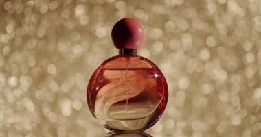 Pembe şapkalı zarif kırmızı parfüm şişesi ışıldayan altın bir arkaplanda fotoğraflanmış, lüks ve sofistike bir duyguyu çağrıştırıyor. Altın Bokeh Arkaplanlı Parfüm Şişesi