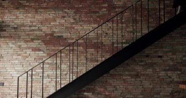 Siyah merdiveni olan modern bir dairede eski tuğla renkli duvar, kadın evin ikinci katından evin merdivenlerinden iner. İç yapı, merdivenli tuğla duvar arkaplanı..