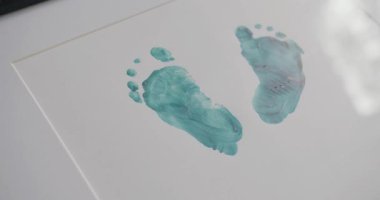 Çizim için yaratıcı bir fikir. Gri yüzeyde yeşil boyayla ustalıkla işlenmiş insan ayak izleri. Renkli akrilik boya ve tuval üzerindeki ayak izlerinin büyüleyici bileşimi. Bebek ayağı..