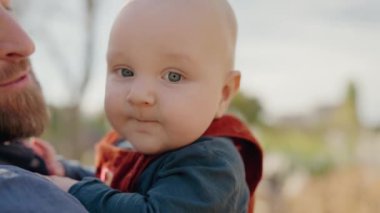 Bir baba ve bebeği arasında geçen hassas bir an güneşli bir açık hava ortamında, mutluluğu ve aile bağını gösteriyor. Neşeli Baba, güneşli bir günde Sevimli Bebeği Dışarıda Tutuyor
