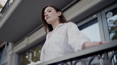 Şık beyaz bluzlu profesyonel bir kadın şehir caddesinde güven içinde duruyor. Dengeli ifadesi ve şık giyimi gündelik zarafet ve şehir yaşam tarzının bir karışımı olduğunu gösteriyor..