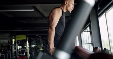 Odaklanmış genç bir adam, antrenmanına dalmış, geniş pencereli ve çeşitli ekipmanlı modern bir spor salonunda koşu bandında koşuyor. Modern Spor Salonu 'ndaki Koşu Değirmeninde Koşan Odaklanmış Sporcu